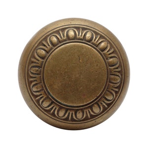 May include: A round, brass door knob with a decorative, raised, circular design around the edge.