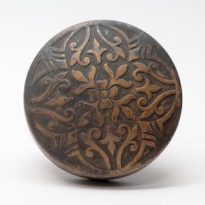 May include: A round, brass door knob with a decorative, embossed floral pattern.