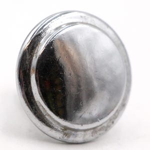 Peut inclure: Un bouton rond argenté avec un motif de cercle concentrique surélevé. Le bouton a une finition lisse et polie.