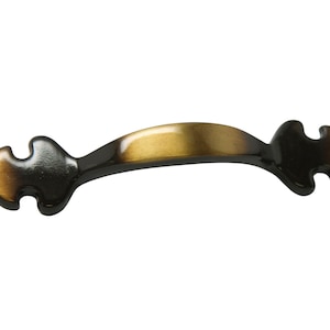 Puede incluir: Un tirador de armario de metal negro y dorado con un diseño decorativo y ornamentado. El tirador tiene una forma curva y un centro ligeramente elevado.