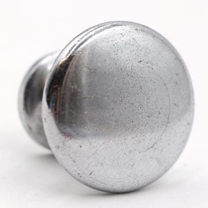 May include: A silver metal knob with a round, slightly textured surface. The knob has a small, raised lip around the edge.