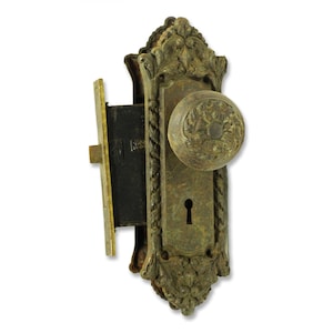 Può includere: Pomo per porta in ottone antico con un buco della serratura e dettagli decorativi. Il pomo ha un design decorativo ed è fissato a una piastra in ottone.