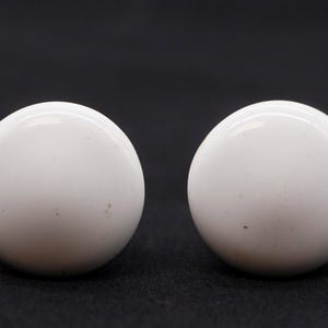 May include: Two white ceramic round knobs with a slightly textured surface.