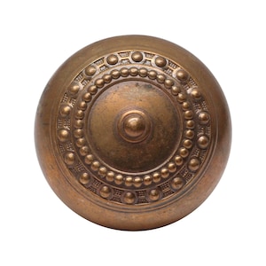 Peut inclure: Une poignée de porte ronde en laiton avec un motif circulaire décoratif en relief. La poignée a une surface texturée et un centre légèrement bombé.