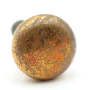 May include: Close-up of a vintage brass doorknob with a weathered, aged appearance. The knob has a rounded shape with a tarnished gold finish and visible rust-colored patches, suggesting age and use. The background is white.