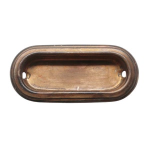 Puede incluir: Un tirador de puerta ovalado de latón con un borde biselado y una superficie lisa ligeramente desgastada.