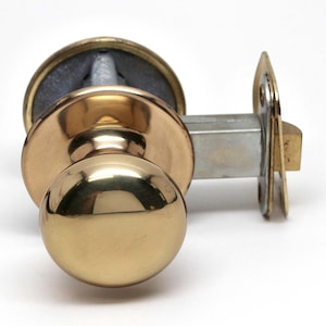 May include: A polished brass door knob with a round, smooth handle. The knob is attached to a silver metal latch.