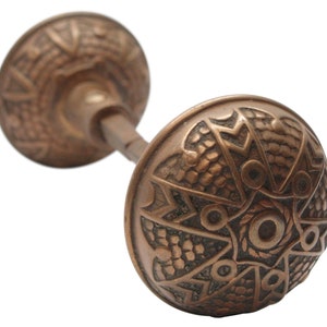May include: A vintage, ornate, copper door knob with a detailed, geometric design. The knob is made of solid metal and has a classic, antique look.