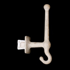 May include: White ceramic hook with a rounded top and a single hook at the bottom. The hook is attached to a square base with a small white plastic piece on the side.