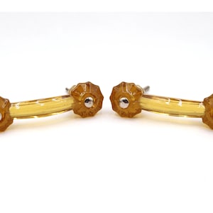 Könnte beinhalten: Zwei bernsteinfarbene Schrankgriffe mit einem blütenförmigen Design an jedem Ende. Die Griffe haben einen klaren, gebogenen Griff und silberfarbene Beschläge. Ideal zum Aktualisieren von Möbeln. Jede Griff ist etwa 10 cm lang.