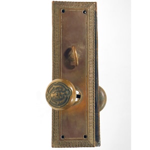 May include: A brass door knob set with a decorative border and a keyhole. The knob has a raised design.
