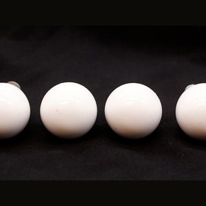 May include: Four white ceramic knobs with a smooth, glossy finish. The knobs are round and have a slight shine.