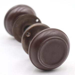 May include: Close-up of antique door knobs. The knobs are a dark brown color with a round shape and a circular base. The metal base is a bronze color. The knobs are arranged in a row, with the closest knob in focus.