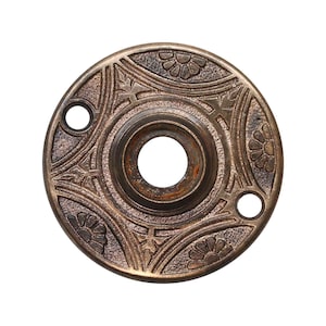 May include: A round, ornate, brass door knob escutcheon with a decorative floral design.