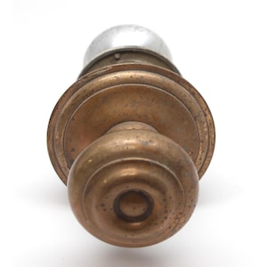 May include: A brass door knob with a round, ornate design. The knob has a silver-colored center.