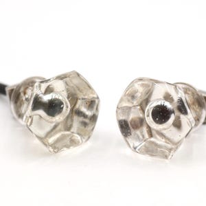 May include: Two clear, hexagonal glass cabinet knobs with a faceted surface and a central circular protrusion. Each knob features a dark metal mounting screw extending from the back, designed for attachment to furniture or cabinetry doors.