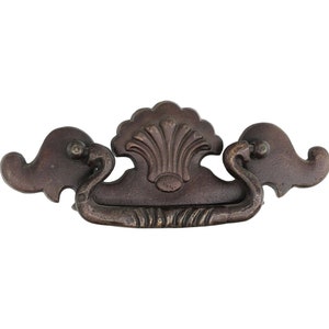 May include: A brown metal drawer pull with a decorative shell design in the center. The pull has a curved shape and two decorative ends.