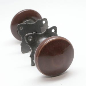 May include: Three brown ceramic door knobs with metal back plates. The knobs are round and have a glossy finish.