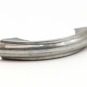 Puede incluir: Un tirador de puerta de armario de metal plateado con forma curva y diseño acanalado.