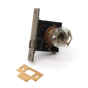 May include: A vintage brass door knob with a clear glass handle. The knob is attached to a brass plate with a keyhole. The knob is in good condition with some signs of wear.