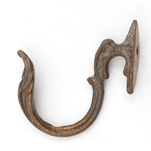 Puede incluir: Gancho de pared ornamental de color bronce con un diseño curvo. El gancho presenta un patrón decorativo en espiral y una placa de montaje con un solo agujero. El metal tiene una apariencia desgastada, lo que sugiere un estilo antiguo o vintage.
