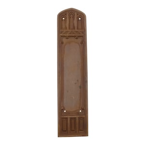Puede incluir: Una placa de puerta de metal marrón con un diseño ornamentado. La placa es rectangular con un arco puntiagudo en la parte superior. El diseño presenta una serie de arcos y cuadrados.