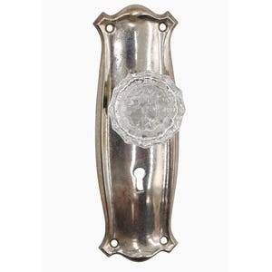 May include: A silver door knob with a clear glass crystal knob. The knob has a keyhole and is attached to a rectangular plate.