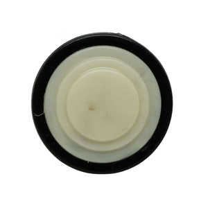 May include: A round, bottle stopper with a black rubber ring, a white plastic ring, and a cream-colored center. The stopper is designed to seal bottles and preserve contents.