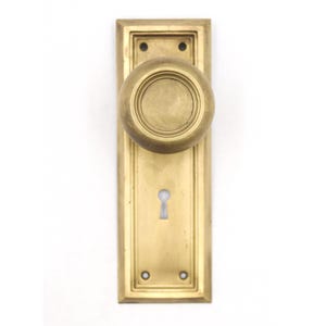 Può includere: Un set di pomelli per porta in ottone con un pomello sferico rotondo fissato su una piastra rettangolare. La piastra presenta un bordo a gradini, due fori per le viti in alto e in basso e un'apertura centrale per la serratura.