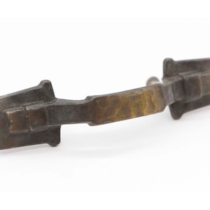 May include: A rustic, antique-style bronze cabinet pull with a simple, curved design. The pull has a slightly textured finish and a subtle aged patina.