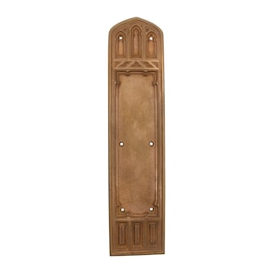 Puede incluir: Una placa de puerta decorativa de latón con una parte superior arqueada y detalles intrincados. La placa tiene una forma rectangular y un acabado liso y cepillado.