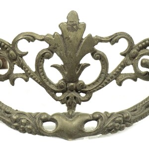 May include: Ornate antique brass drawer pull with a decorative floral and scroll design. The handle is a curved shape with detailed embellishments, perfect for vintage furniture restoration projects.