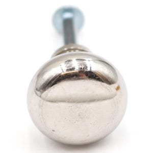 Peut inclure: Gros plan sur un bouton en métal argenté brillant de forme sphérique. Une tige filetée s'étend du bouton, menant à une sphère plus petite, bleu clair. Le bouton est probablement pour une armoire ou un tiroir.