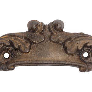 May include: A cast iron drawer pull with a decorative, ornate design. The pull is finished in a dark brown color with a distressed look.