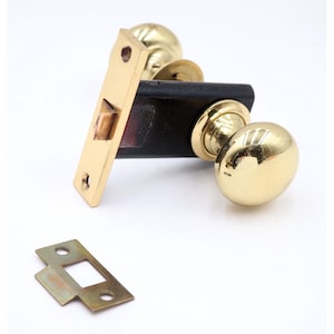 May include: A gold-colored door knob set with a rectangular strike plate and a separate latch plate. The door knob has a rounded shape and a shiny finish. The set is designed for a door.