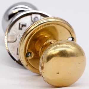 May include: A polished brass door knob with a round, smooth handle. The knob is attached to a round, flat plate with a decorative edge.