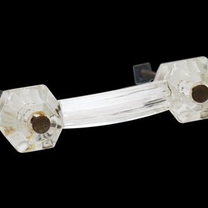 Könnte beinhalten: Ein klarer Glas-Schranktürgriff mit zwei achteckigen Knöpfen. Die Knöpfe haben eine leicht mattierte Oberfläche und eine Schraube aus Metall in der Mitte.