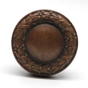 Puede incluir: Un pomo de puerta redondo de bronce con un diseño decorativo de corona.