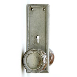 Può includere: Una maniglia per porta vintage in argento con un buco della serratura e una piastra decorativa. La maniglia ha un aspetto usurato e invecchiato.