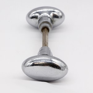 May include: A pair of oval-shaped, chrome door knobs with a metal rod connecting them.
