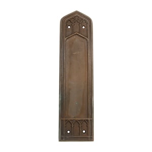 Könnte beinhalten: Eine lange, rechteckige, bronzene Türplatte mit einem gewölbten oberen Rand und aufwendigen Verzierungen. Die Platte hat zwei Löcher zur Befestigung.