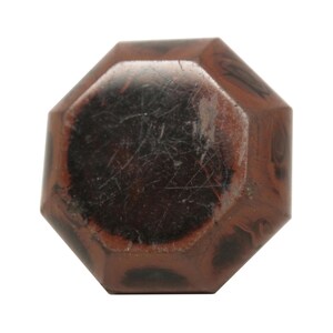May include: An octagonal bottle stopper with a dark brown center and a lighter brown, patterned exterior. The stopper has a glossy finish and appears to be made of a solid material.