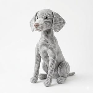 May include: A crocheted gray dog with a seated posture. The dog has long, floppy ears, a brown nose, and a small tail. The dog is made of a textured yarn and is sitting on a white background.