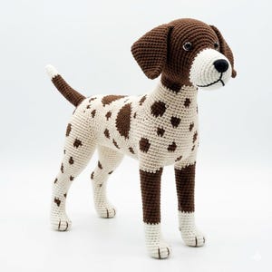 Puede incluir: Un perro de ganchillo hecho a mano en posición de pie. El perro tiene un cuerpo blanco con manchas marrones, patas, orejas y cola marrones. La nariz del perro es negra y los ojos son oscuros. El perro de ganchillo es un artículo decorativo.