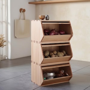 May include: A three-tiered wooden storage unit with angled openings, filled with red onions, potatoes, and other items. The natural wood finish complements the kitchen setting. A small bowl and decorative object sit on top.