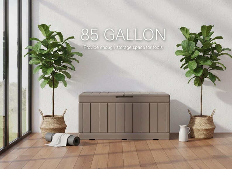 May include: A large, taupe-colored storage chest with a hinged lid, providing 85 gallons of space. The text on the wall reads "85 GALLON" and "Provide enough storage space for tools". Two potted plants flank the chest, with a rolled yoga mat in front.