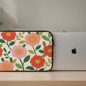 May include: A floral laptop sleeve with a cream background and a pattern of red, pink, and yellow flowers with green leaves. A silver laptop is next to the sleeve.