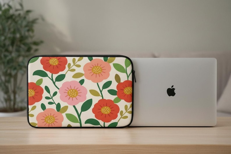 May include: A floral laptop sleeve with a cream background and a pattern of red, pink, and yellow flowers with green leaves. A silver laptop is next to the sleeve.