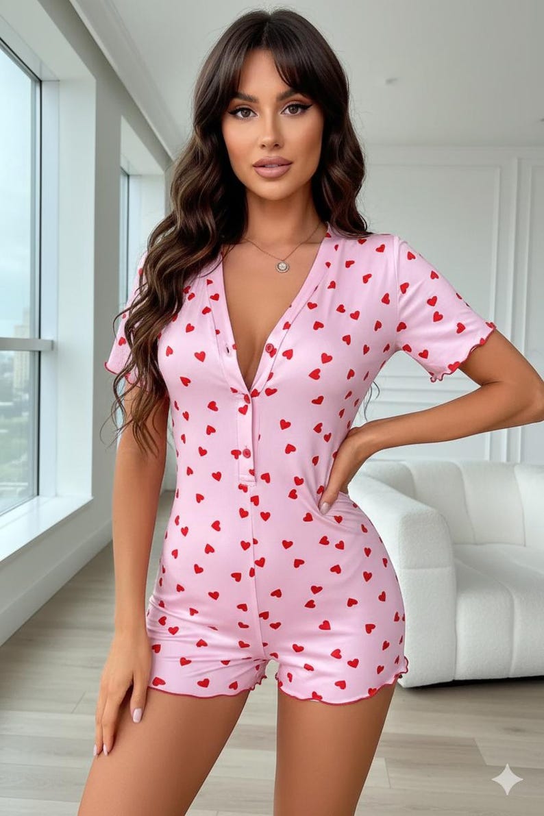 Puede incluir: Mono rosa con estampado de corazones rojos. El mono de manga corta presenta un escote en V y una botonadura frontal. Los bordes de las mangas y los pantalones cortos tienen un ribete festoneado. La prenda est&aacute; hecha de una tela suave y ligera.