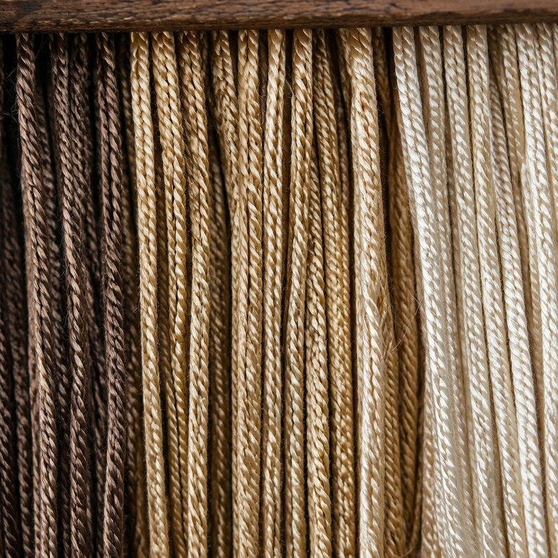 May include: Close-up of several strands of twisted cord in varying shades of brown, tan, and cream. The cords are arranged vertically, creating a textured surface. The cords are likely made of natural fibers.